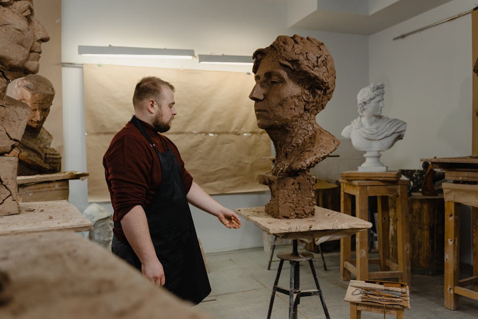A sculptor working on a clay bust in an art studio, surrounded by sculptures and tools.