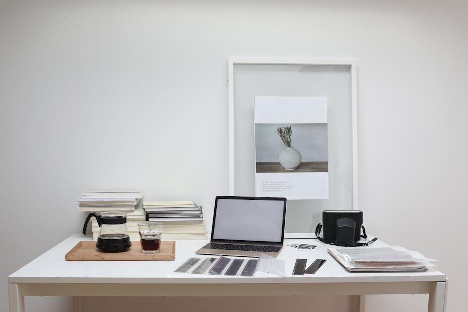 Modern laptop with blank screen arranged with retro filmstrips photo camera and framed picture placed on table near coffee and stack of books
